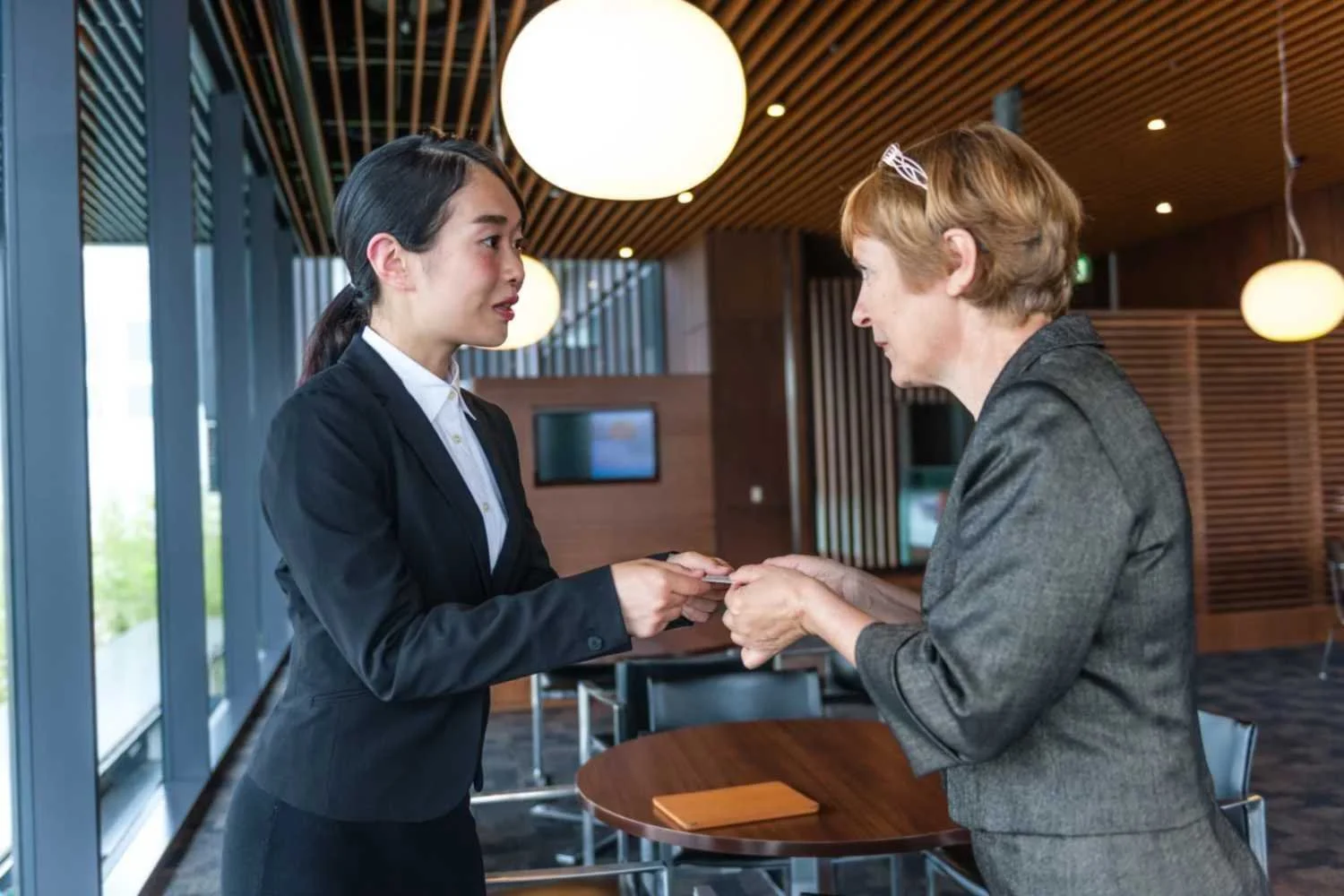 Two professionals exchanging business cards during cultural exchange meeting in office San Jose, CA