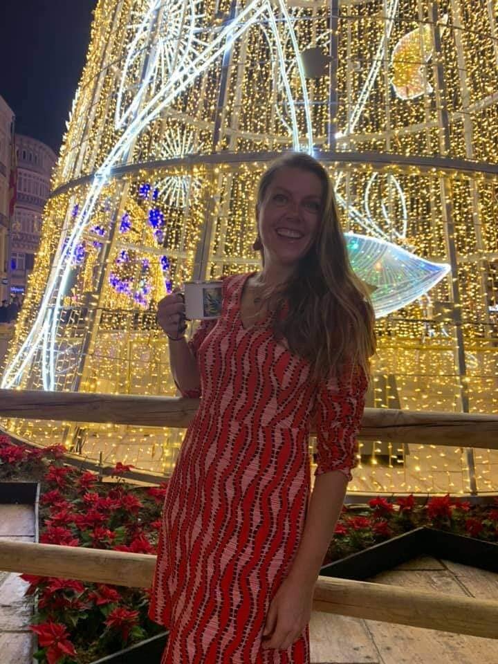 Artist Pigsy's wife in a red party dress holding a Pigsy art cup in front of the giant Christmas tree in Malaga Spain on Calle Larios