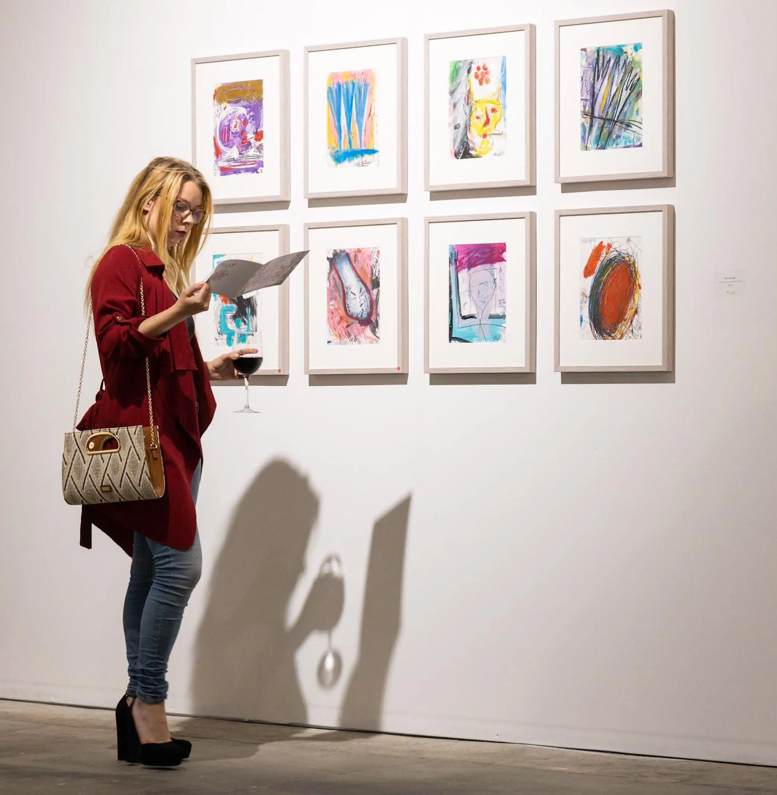 a lady holding a wine glass stands in front of PIGSY framed artworks . The lady's silhouette projects on to the wall
