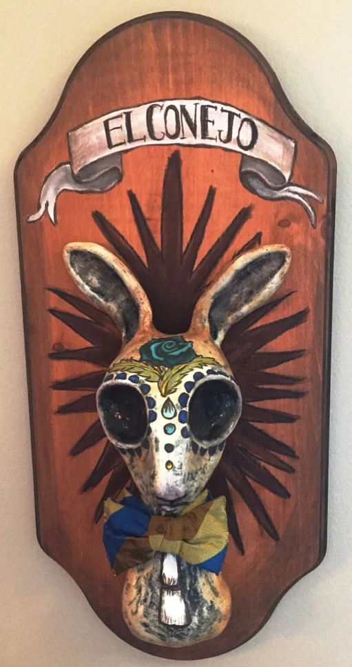 EL CONEJO, DAY OF THE DEAD RABBIT "El Conejo", The Rabbit, was created in the Day of the Dead, Dia de los Muertos style found in Mexican folk art. I hand sculpted him from clay, using no mold. He is hand painted and sealed with matte polyurethane. His bow tie is vintage. He is mounted on a hand painted wood plaque. El Conejo is 18" tall X 9" wide. His head protrudes from the plaque 4" at it's deepest point.