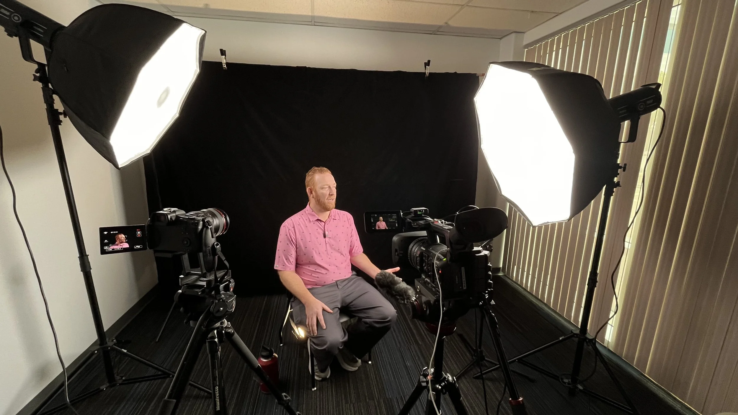 A man sitting in front of a camera and studio lighting, being recorded during an interview or presentation in a professional studio setting.