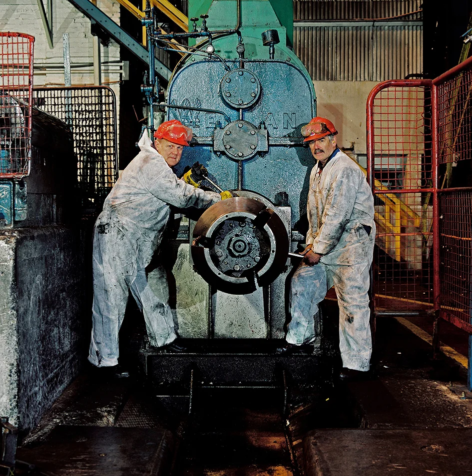 Ray Best (left) - Fitter/Turner - 40 years at the Works Philip Blackmore (right) - Fitter - 46 years at the Works Ray Best... When I started working at the plant, it seemed everybody either had a relation or knew someone who worked there. At that time, 1962, there was a workforce of over 10,000 people. And the Works seemed to dominate the valleys for 24 hours a day. Whenever you met friends or relations socially, the first greeting was always along the lines of “What are you working?” meaning what shift rota you were on. You felt very secure in your job and happy to know your future, at least at that time, was in safe hands. When the works finally closed, everything changed and there was a feeling of doom, which still exists to this day in the valleys. Philip Blackmore... I cannot overstate the camaraderie, and even allowing for the dangers, I loved working there. The Works dominated the town. There could not be many factories where you could get up at 5.50 in the morning on a day shift and clock on at 6.00am. One instance of danger that I recall was on an afternoon shift in the Open Hearth when a ladle crane transferring hot metal to the teeming landing (where the molten metal from the ladle would be poured into ingot moulds) suffered a broken gear-box (hoist) shaft and dropped the ladle containing 180 tonnes of molten steel all over the floor. That no one died was a miracle, although it took a couple of hours for the heart-rate to subside! At the very end I was working for the contracting firm ‘Vinci’ and after the official closure I had 3 months work removing assets that were to be sent to other plants in other countries, mainly Holland and India. I found that I was more than annoyed that other countries could see the advantages of keeping this equipment and we could not! I felt like a grave robber! When I visit Ebbw Vale now, if I am honest, I feel that it is a sad place as its heart is gone and the good living that I had there is not available to others. It really once was a vibrant town.