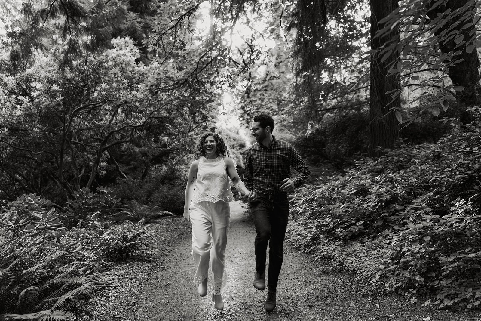 a wedding couple skip through the forest on their engagement session