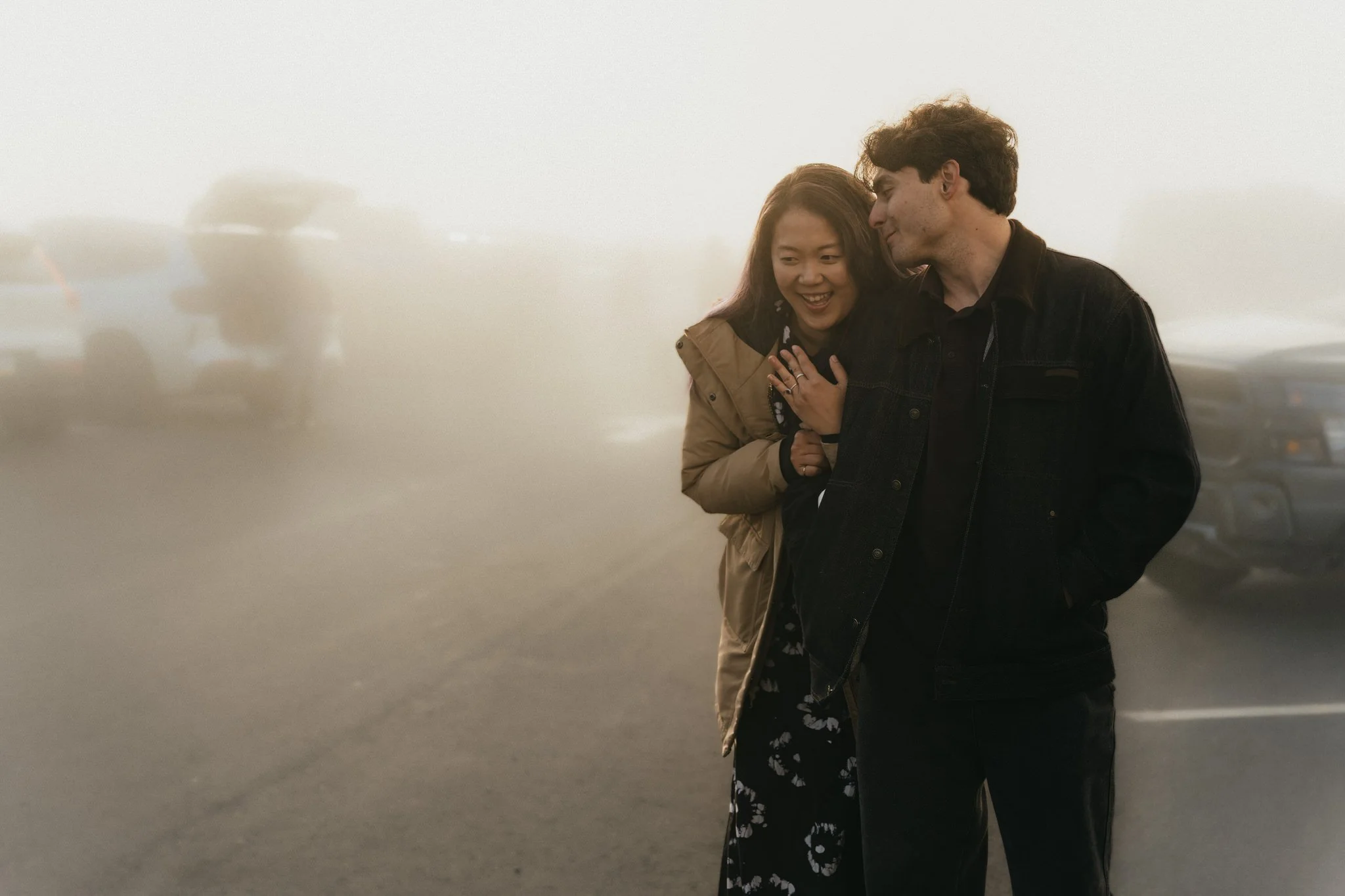 a man and woman stand in a parking lot surrounded by fog at Mount Rainier National Park