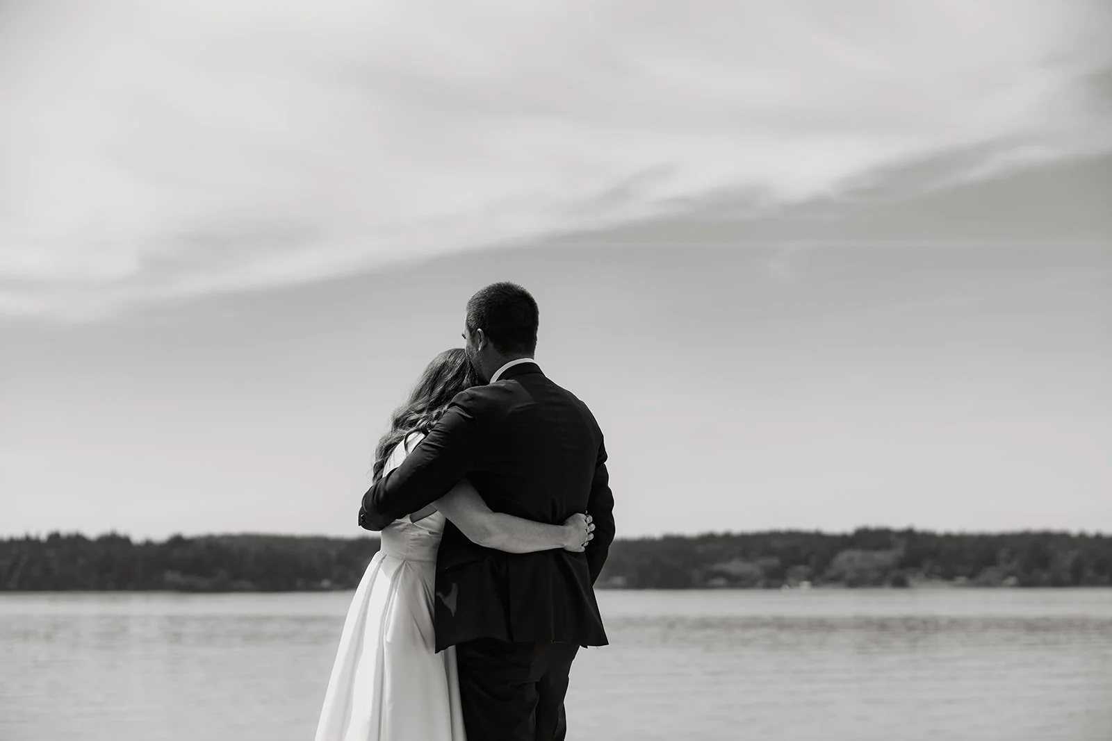 a bride and groom look out to the sea on their wedding day