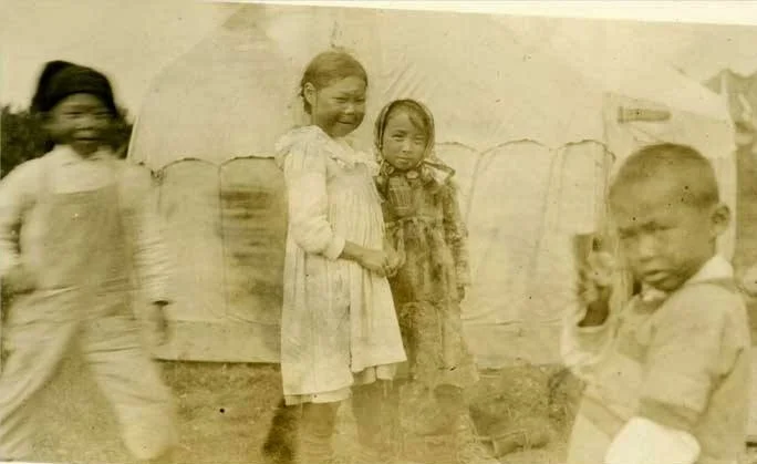 "View of four children, two boys and two girls, in front of a tent at Naknek, Alaska." Caption also reads: "Children orphaned by the flu epidemic at Pawik." Pawik is a variant name for the village of Naknek. UAA-hmc-0186-volume7-6462,&nbsp;from "Ind…