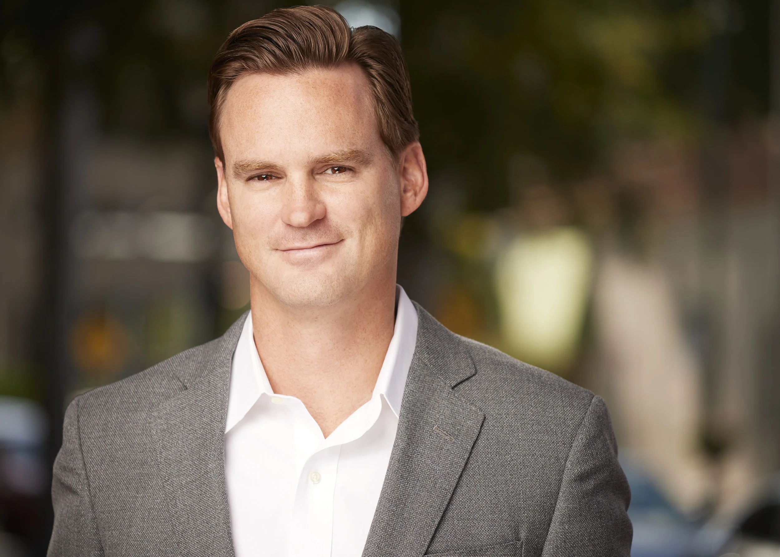 Headshot client wearing a tan sports coat with a white collared shit with no tie.