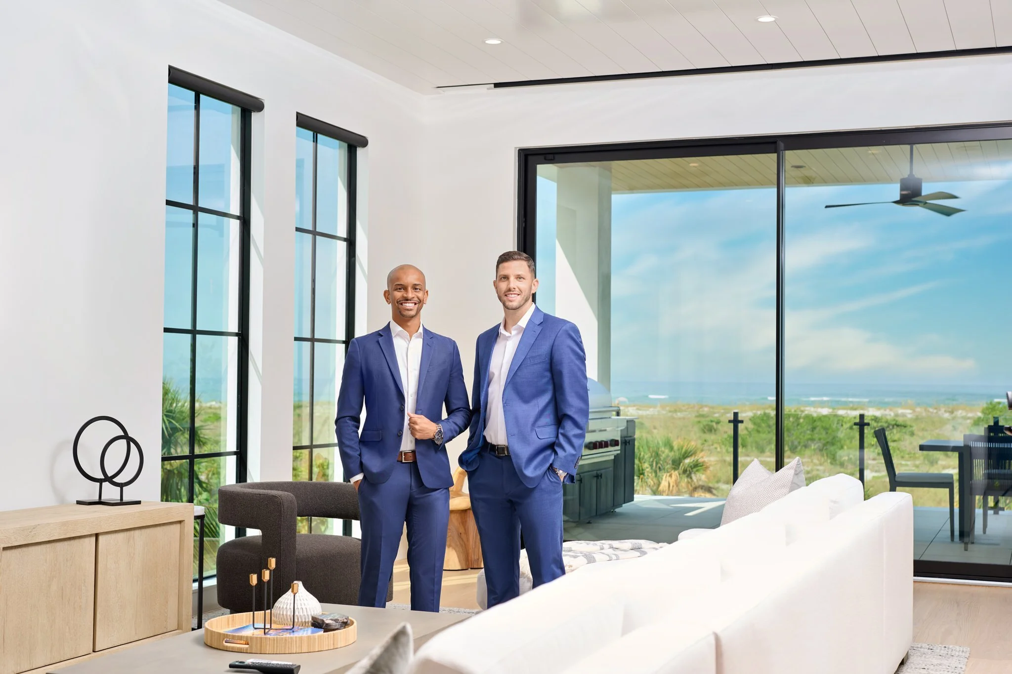 Two real estate professionals in blue suits photographed inside a luxury waterfront home for a Sarasota team branding portrait by SRQ Headshots.