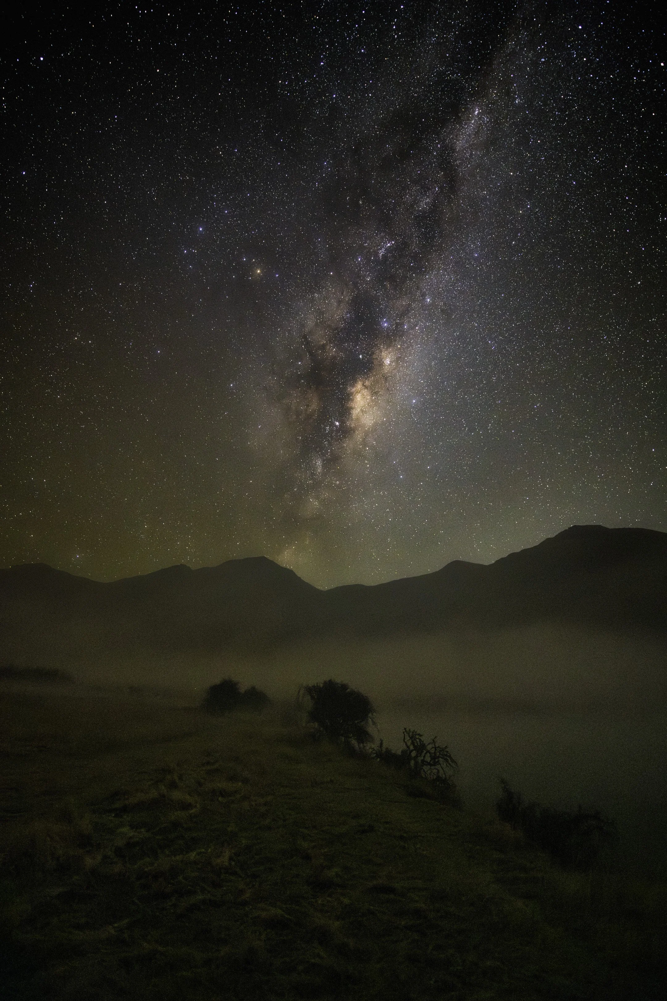 The Milky Way rises above a misty Punamāhaka (Moke Lake) and the surrounding mauka, Queenstown, New Zealand