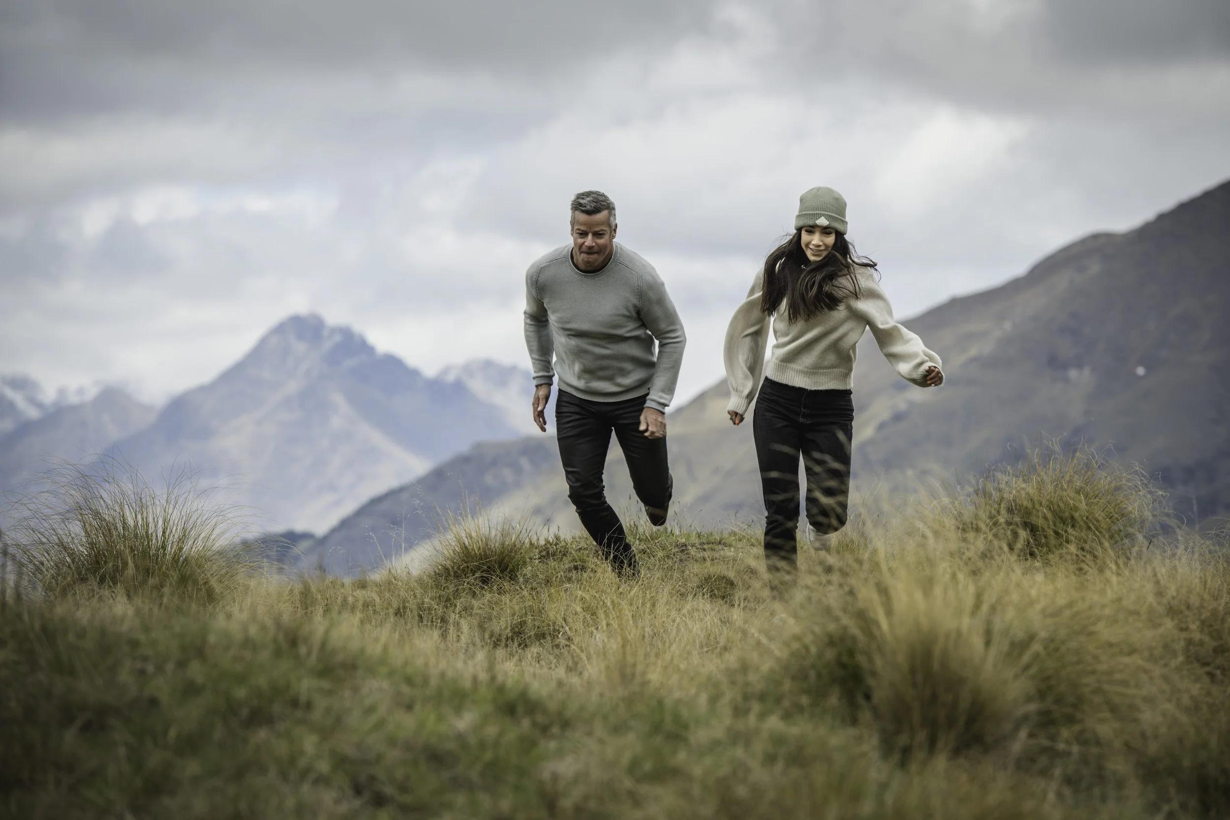 Father and daughter running across a tussock-covered mountainside during a fun family photoshoot, professionally photographed