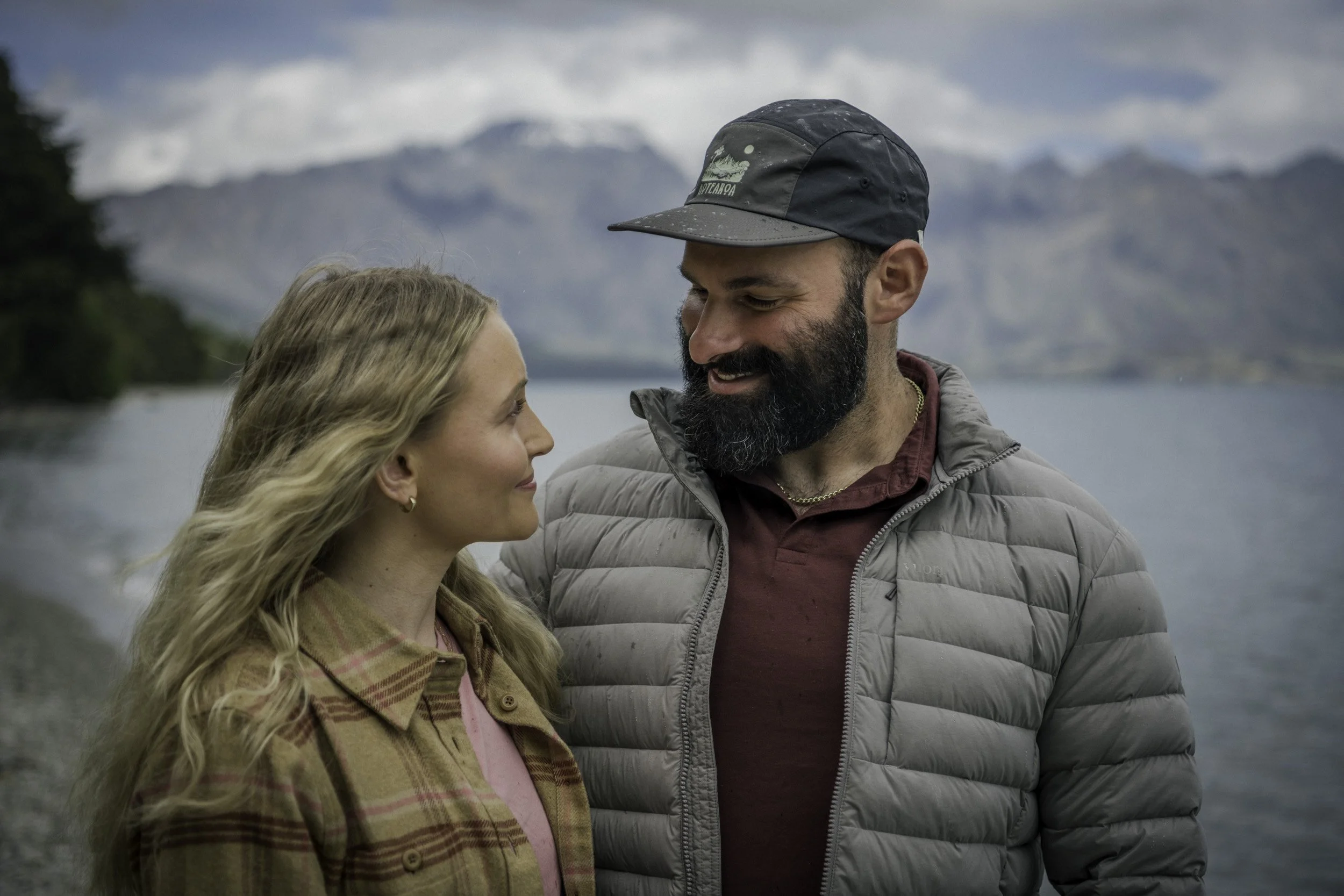 Honeymoon couple walking along Whakatipu Wai Māori shoreline with The Remarkables in the background