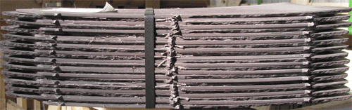 A bundle of 25 plum coloured slates placed underside up. Note the slight concave shape (or camber) of the slates. Once fixed, the slates flatten out creating a positive downward force on underlying slates. This reduces wind driven moisture penetration under the top slate. The capillary action of moisture is also impeded.