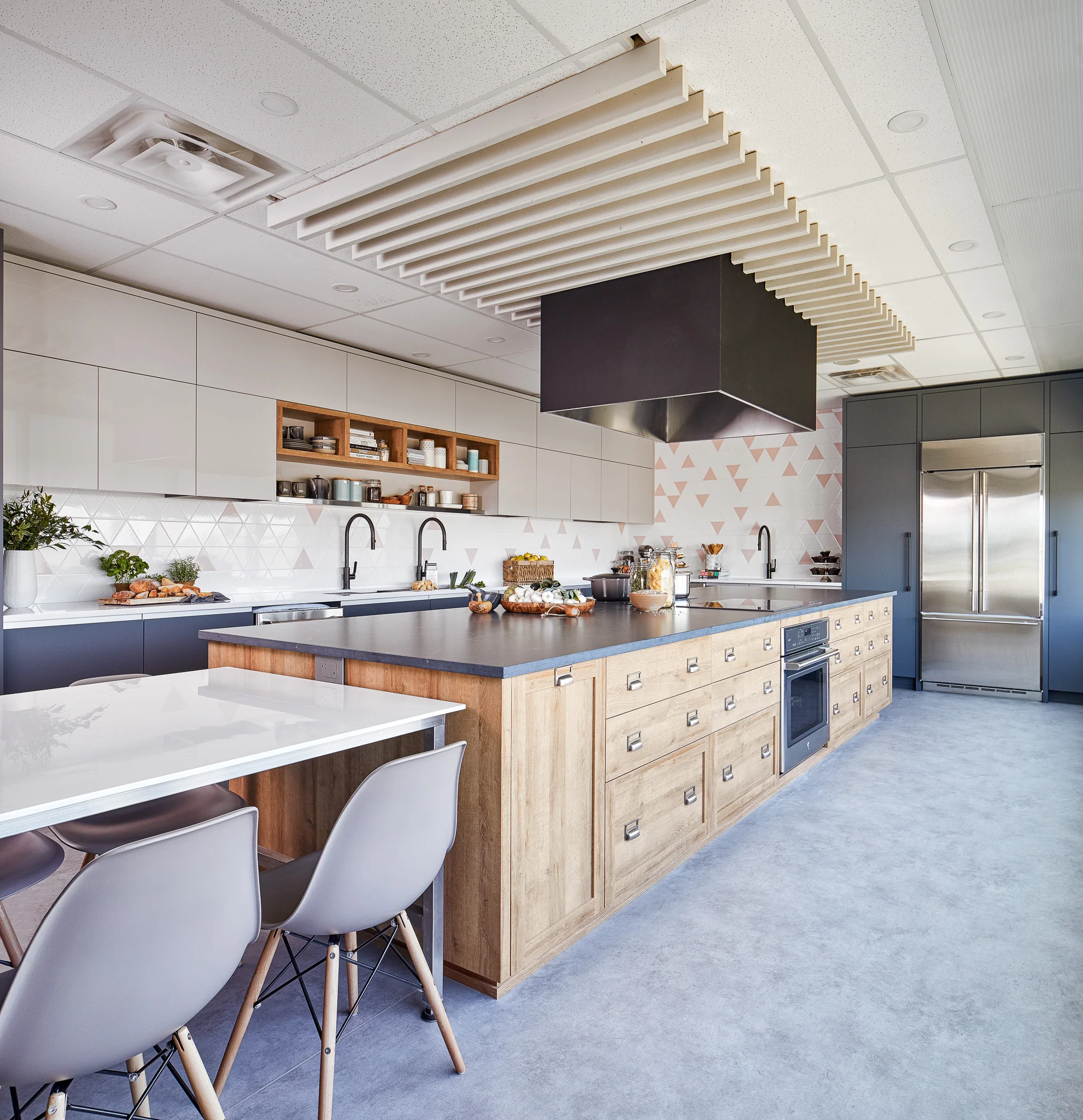Large hood spans over both cooktops located back to back on the island. Hood vent and the painted wood canopy that surrounds it also creates an interesting focal point and breaks up the institutional feeling of the commercial grid ceiling.