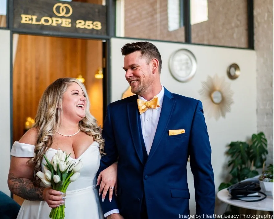 Happy Newlyweds smiling at each other under the Elope 253 sign at the local tacoma wedding chapel