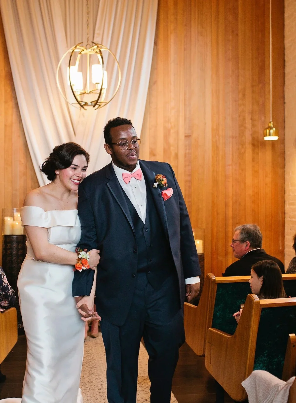 A bride and groom walking down the aisle during a wedding ceremony inside a warmly lit wooden chapel.