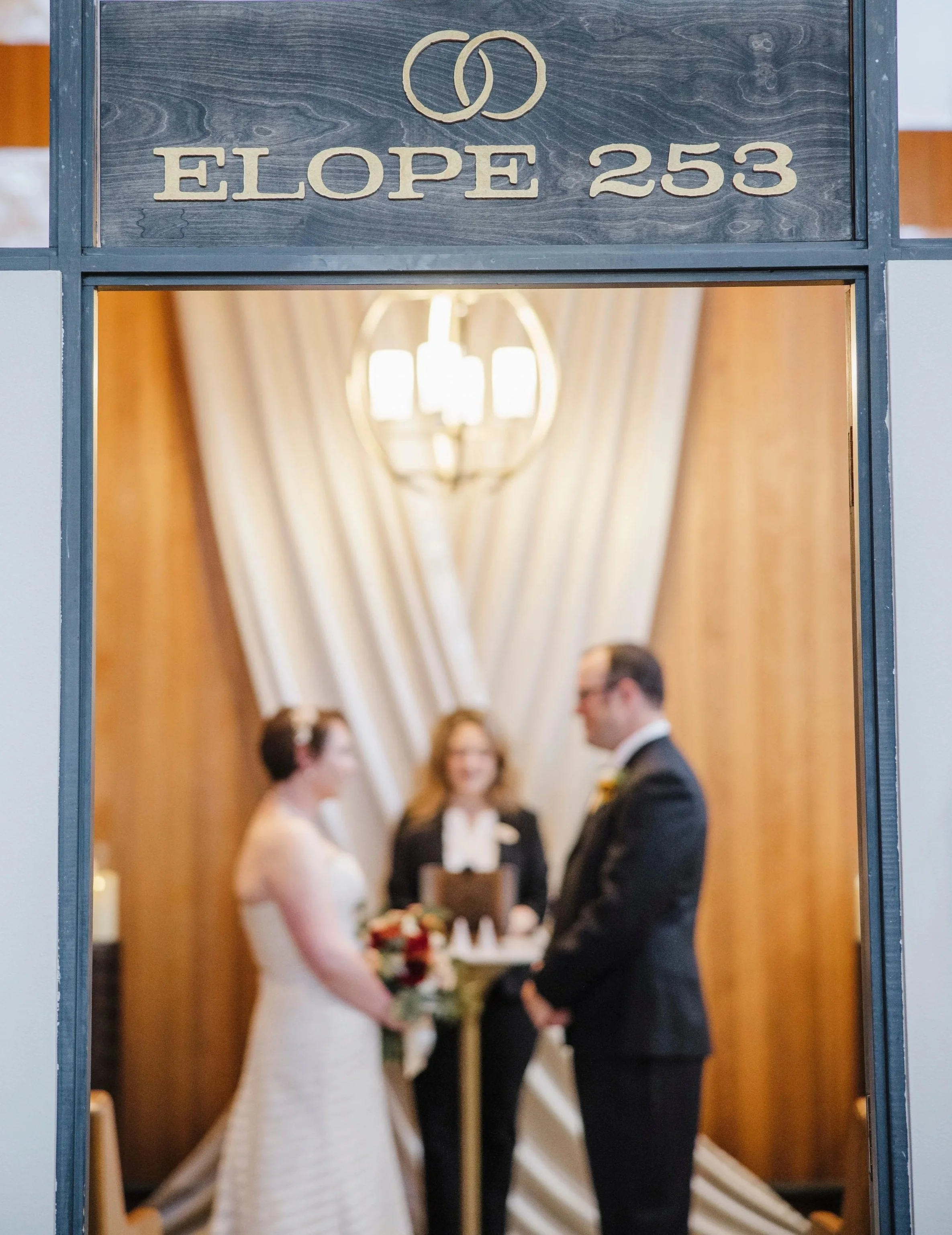 A bride and groom during wedding ceremony with a wedding officiant , guests and wedding decor visible in the background.