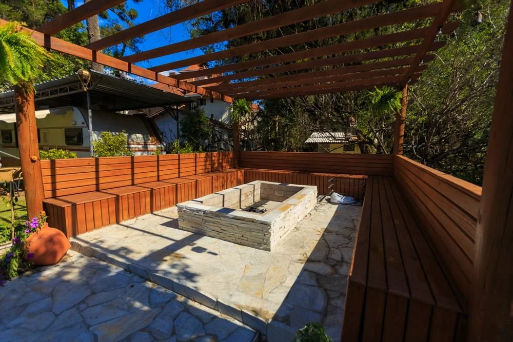 Stone paver patio with a central fire pit, wooden bench seating, and an overhead pergola