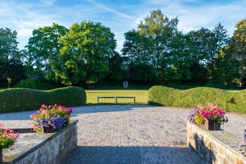 Large paver driveway bordered by hedges and flowers