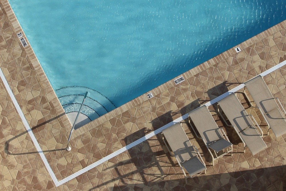 Overhead view of a swimming pool with a patterned stone paver deck, lounge chairs, and a metal pool handrail