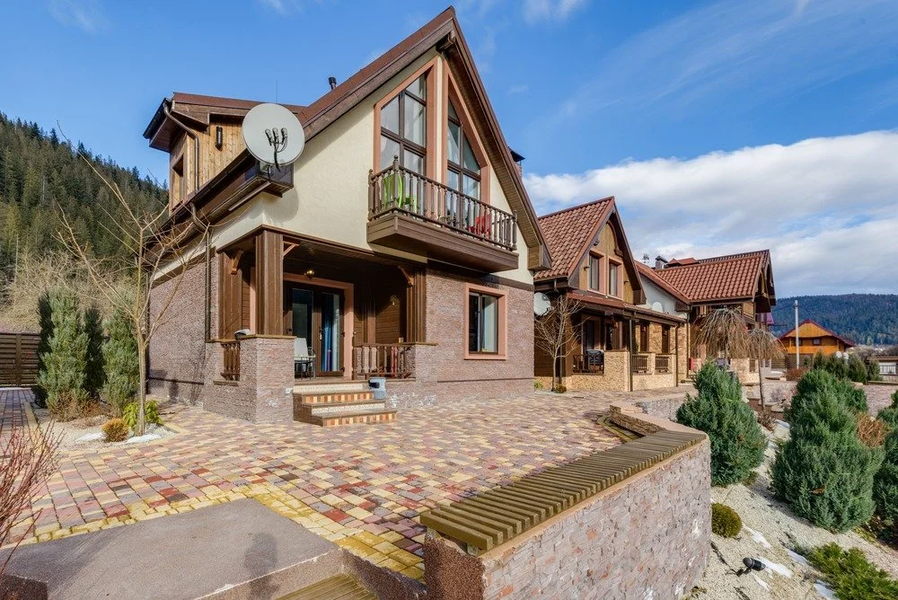 Spacious multicolored paver patio outside a large house with balconies and landscaped gardens