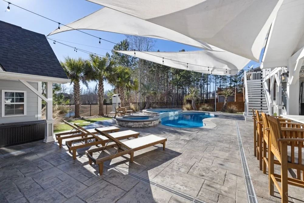 Paved pool patio with lounge chairs and shade sails
