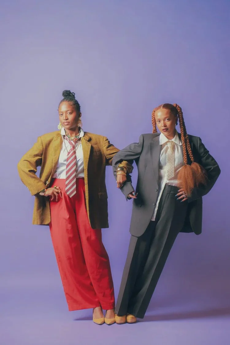 Two women in oversized tailoring and colorful trousers pose against a purple backdrop in Sista Sista. Photography by Yonathan Mesfun.