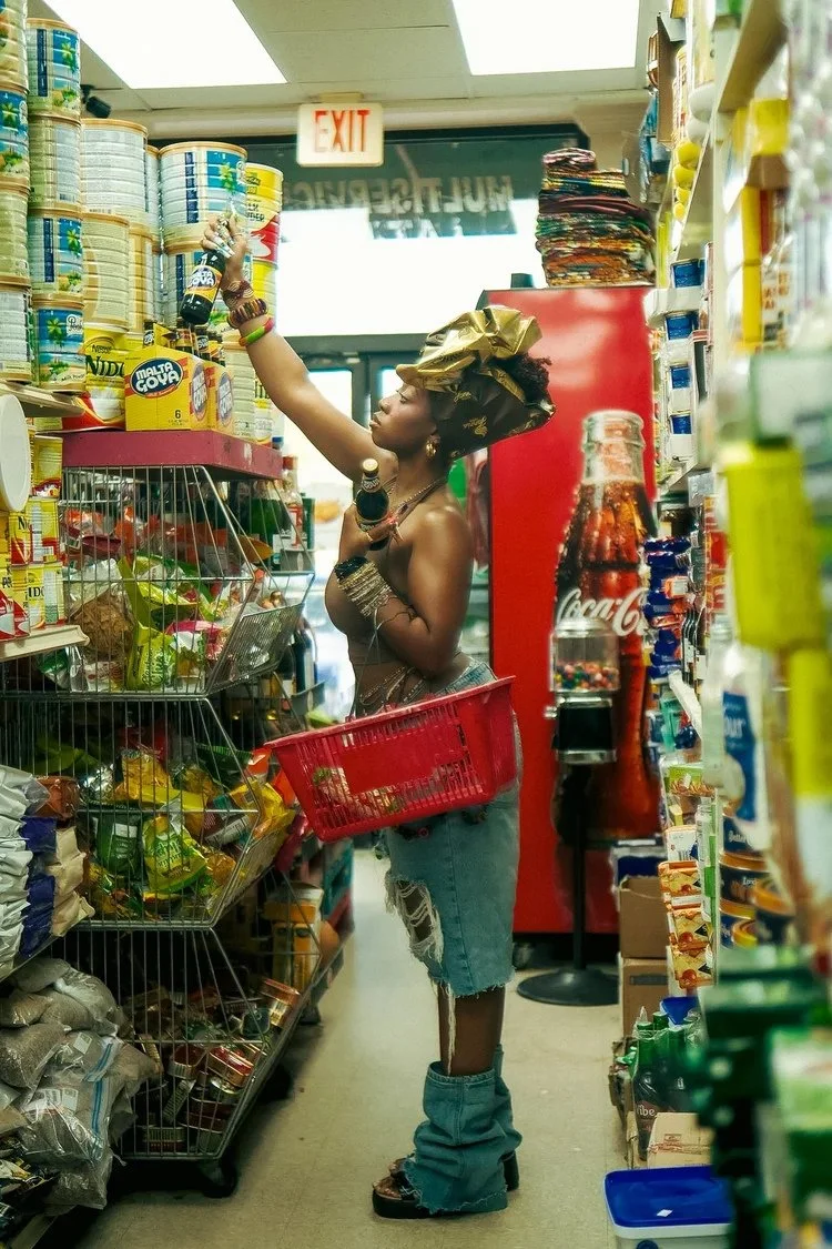Model reaches toward a grocery shelf while holding a red shopping basket in Sierra Leone. Photography by Yonathan Mesfun.