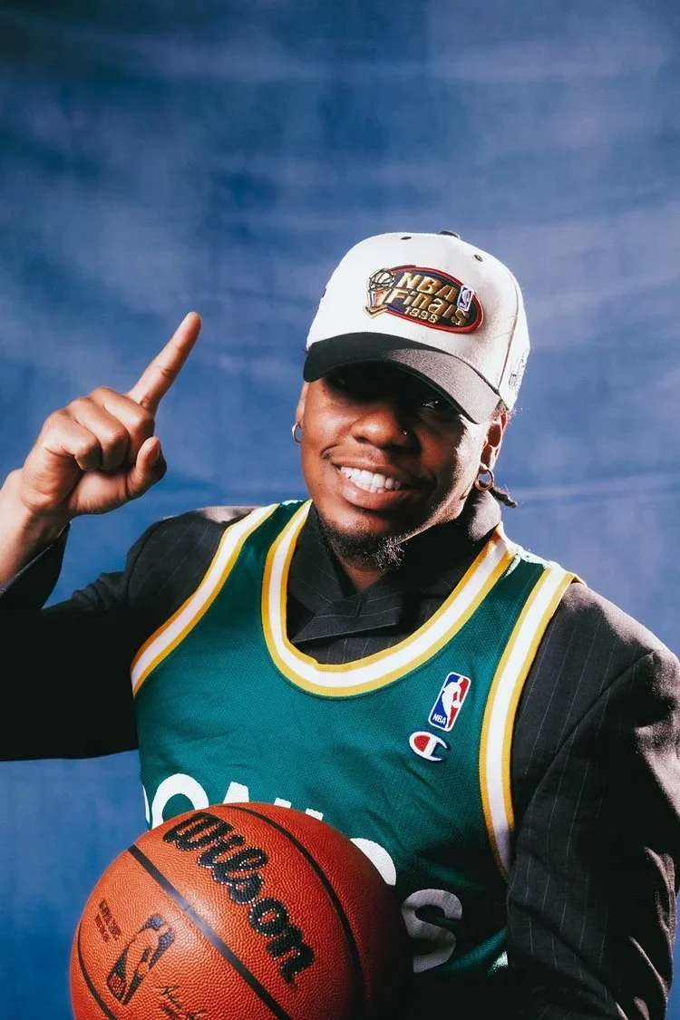 Smiling model in a green basketball jersey and white cap holds a basketball in Draft Day. Photography by Yonathan Mesfun.