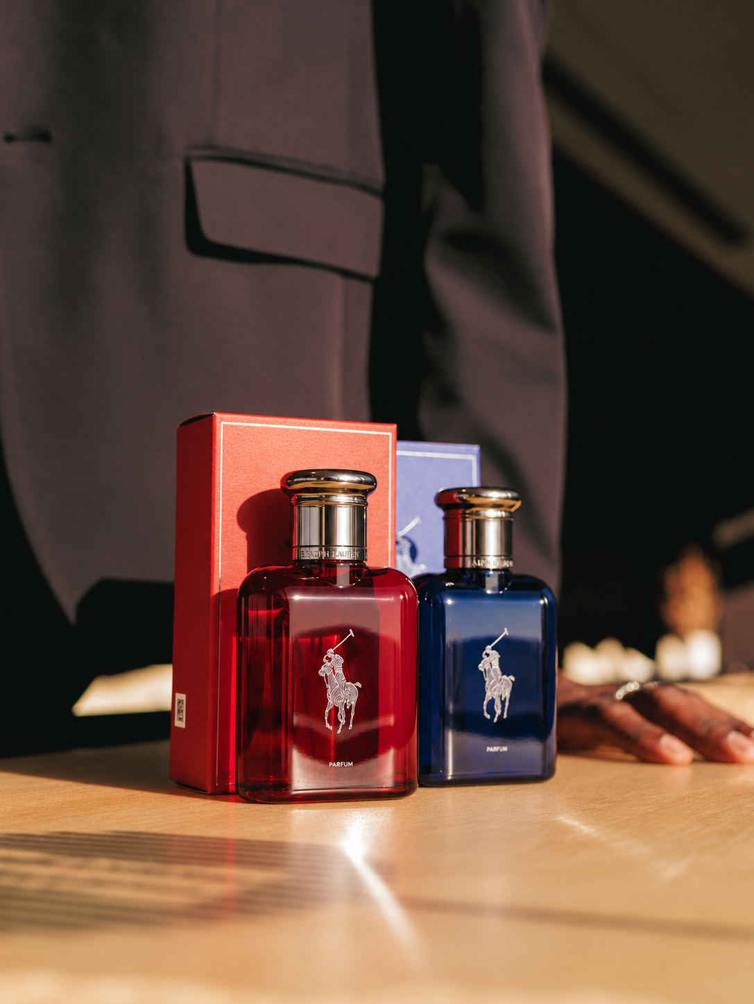 Red and blue Ralph Lauren Polo fragrance bottles stand beside their boxes on a wooden surface.