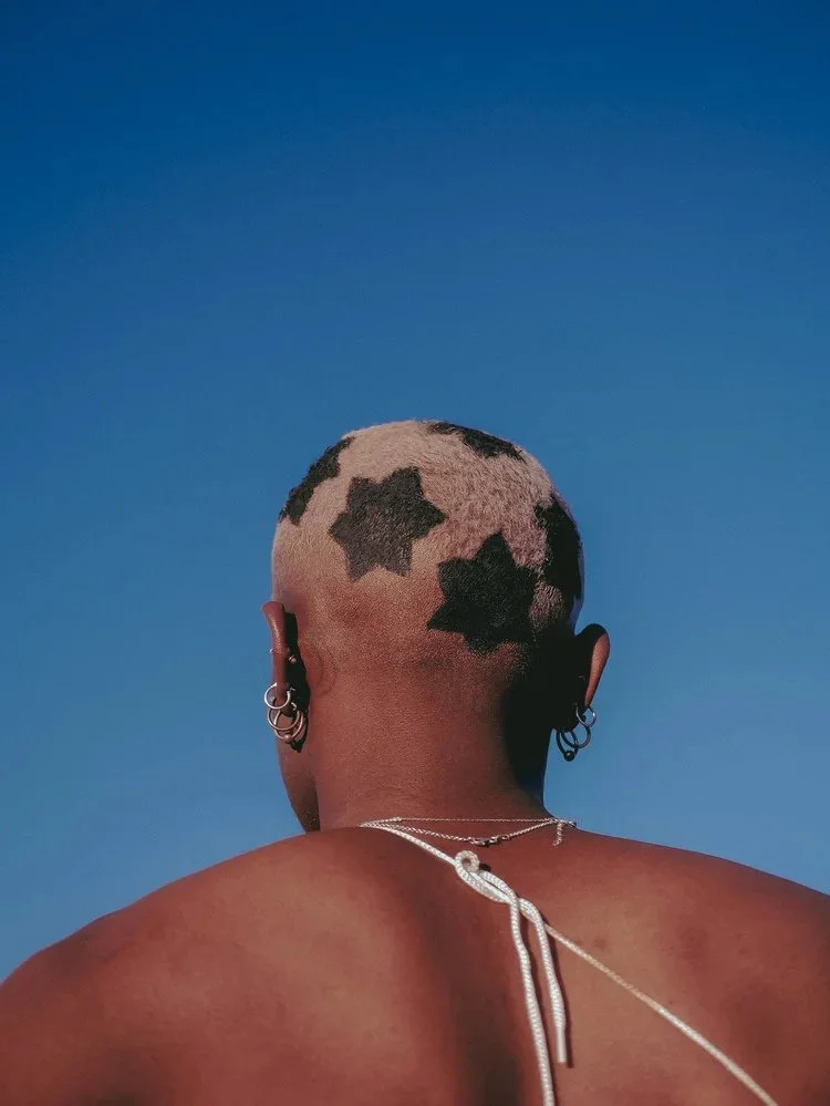 Back view of a model with star-shaped patterns in cropped hair in Bad Bandits. Photography by Yonathan Mesfun.