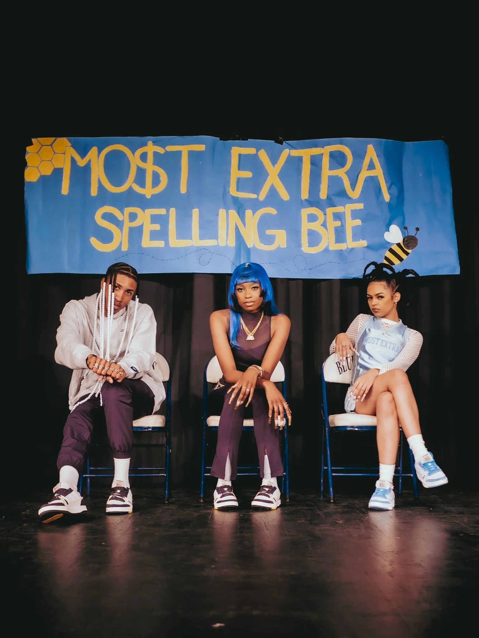 Three seated models below a Most Extra Spelling Bee banner in a Reebok campaign. Photography by Yonathan Mesfun.
