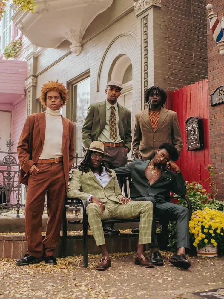 A group in tailored suits gathers outside a neighborhood storefront in Gentlemen. Photography by Yonathan Mesfun.