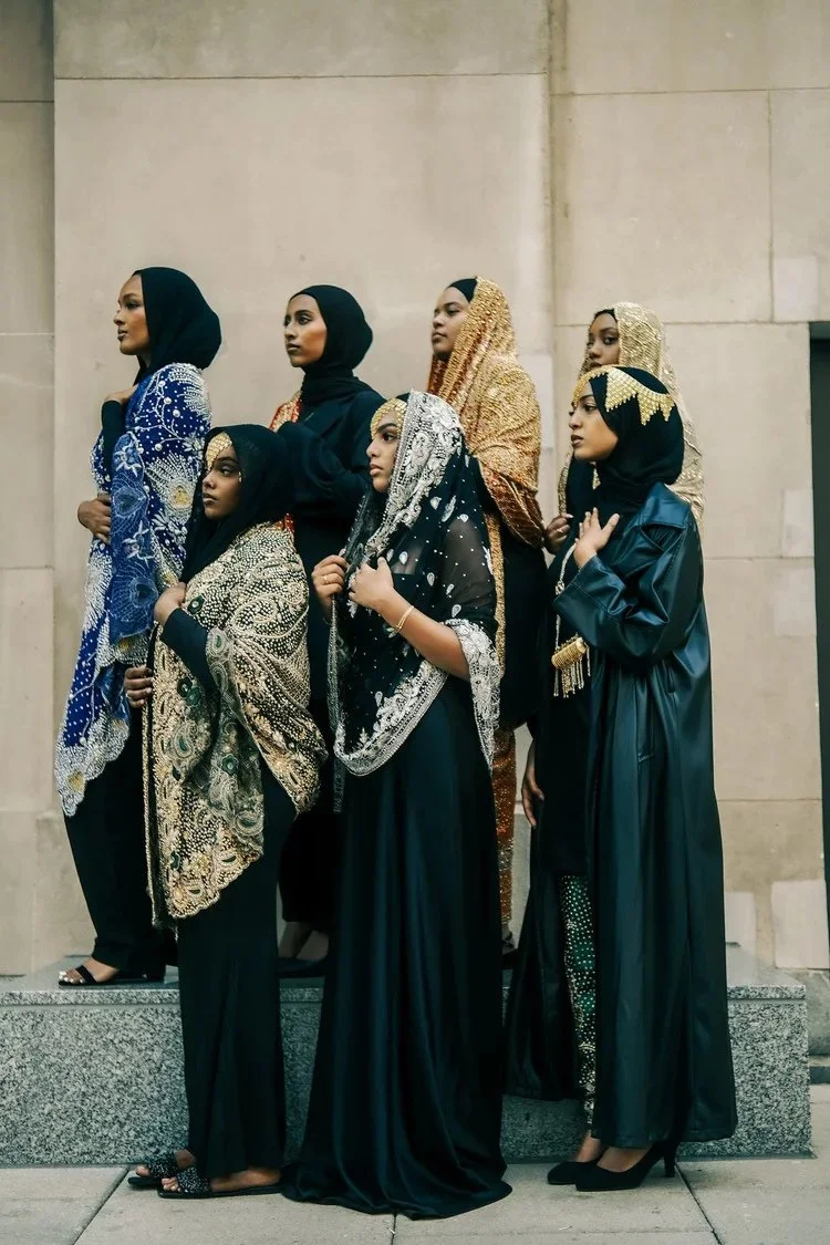 A group of women in embroidered shawls stands against a pale stone wall in A Collected Culture Pt.2. Photography by Yonathan Mesfun.
