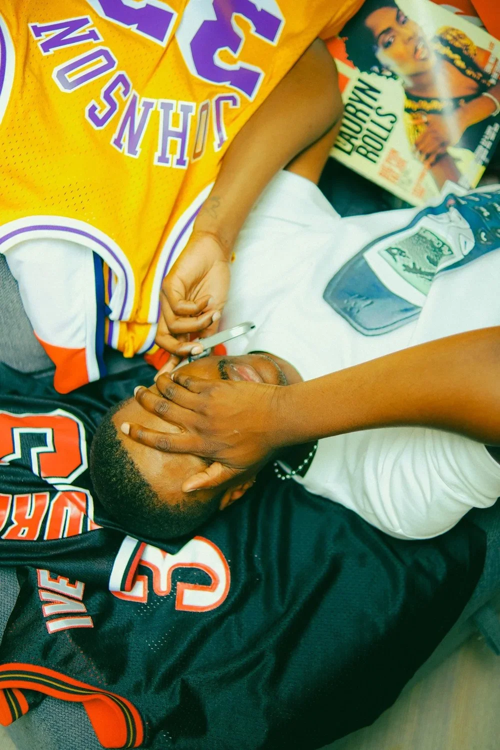 Overhead view of a reclining model surrounded by basketball jerseys and magazines for Rekluse Gallery. Photography by Yonathan Mesfun.
