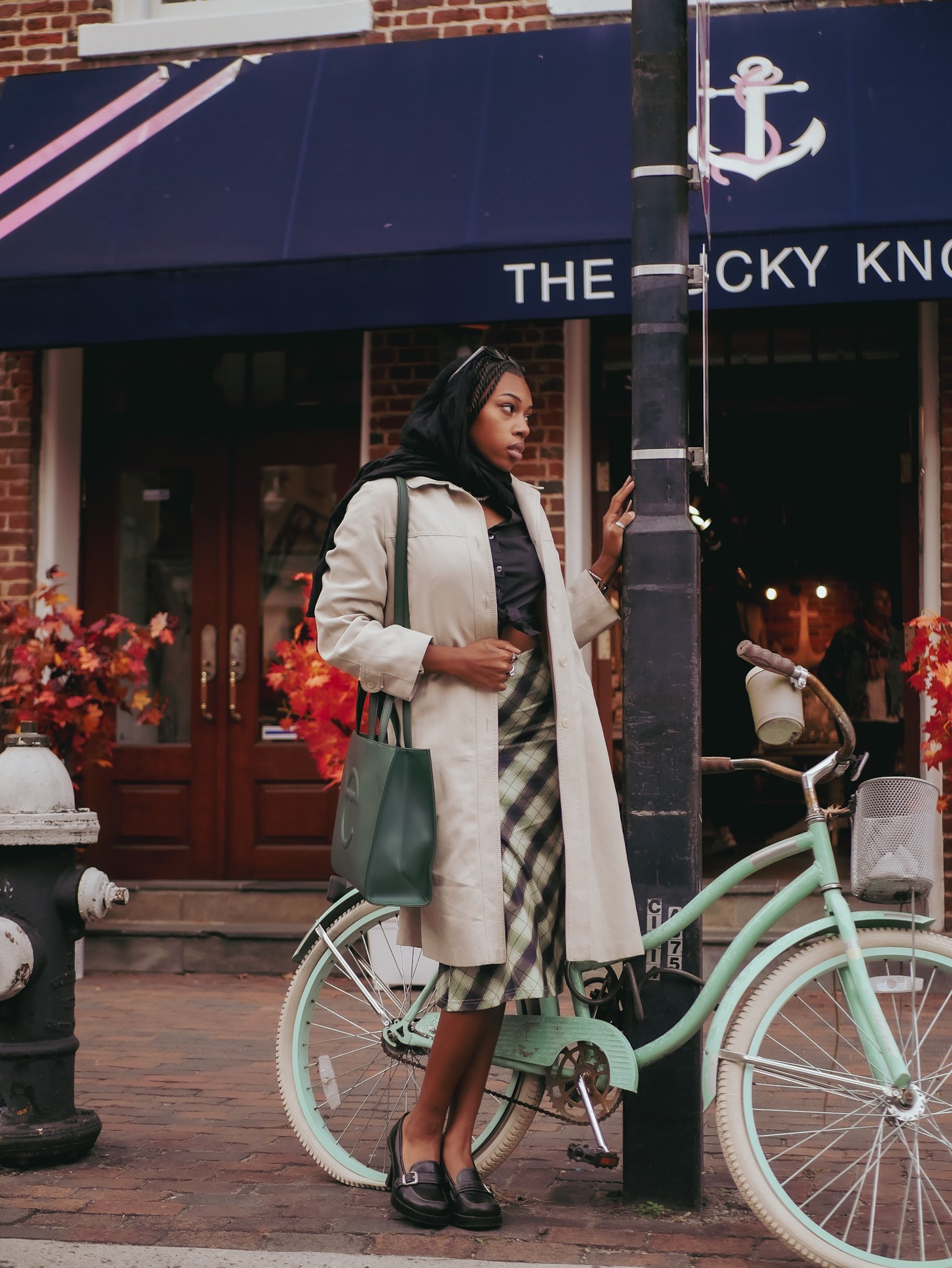 Model holding a green Telfar bag beside a mint bicycle outside a shop. Photography by Yonathan Mesfun.