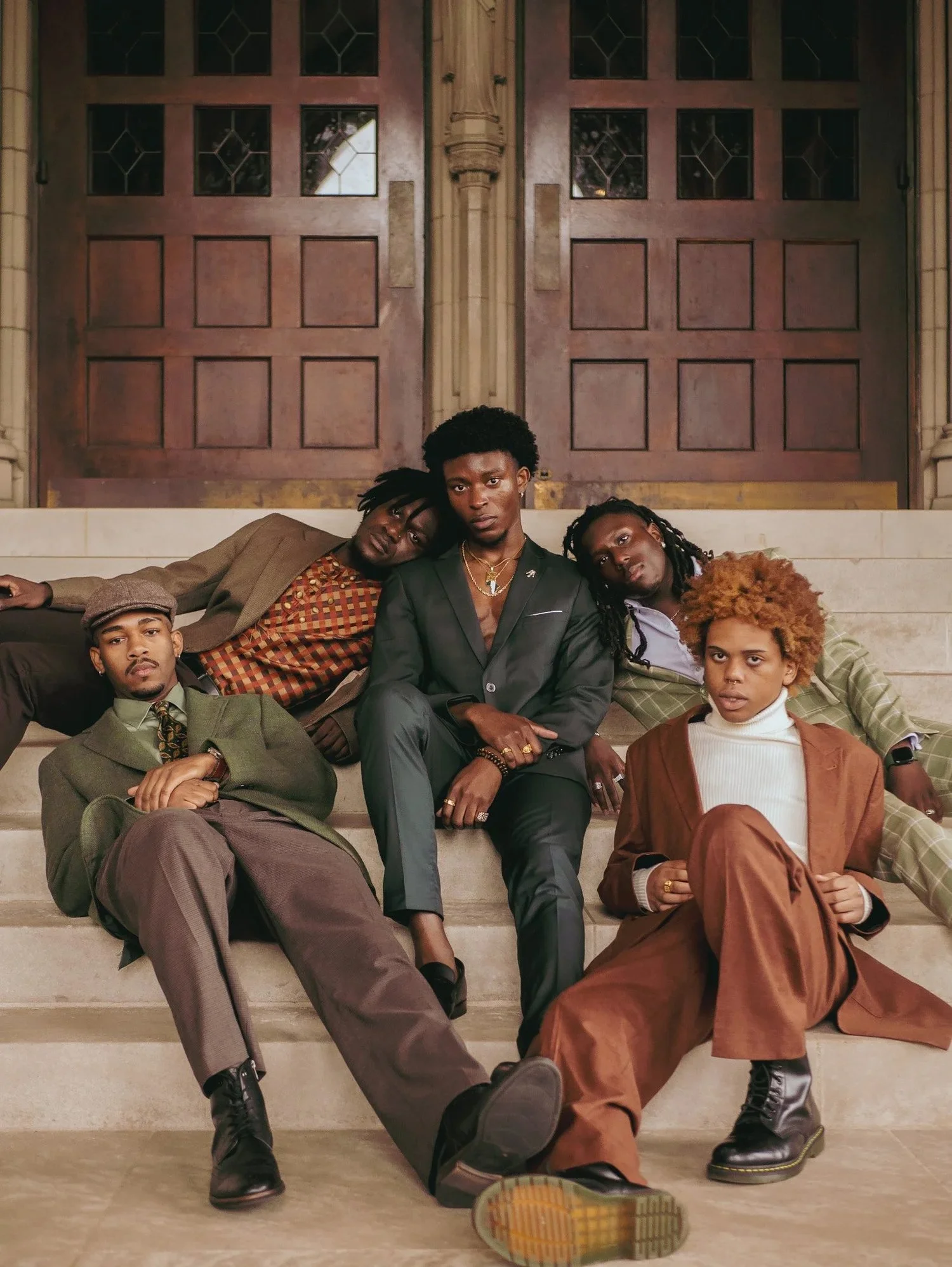 Five models in earth-toned suits lounge on stone steps in Gentlemen. Photography by Yonathan Mesfun.