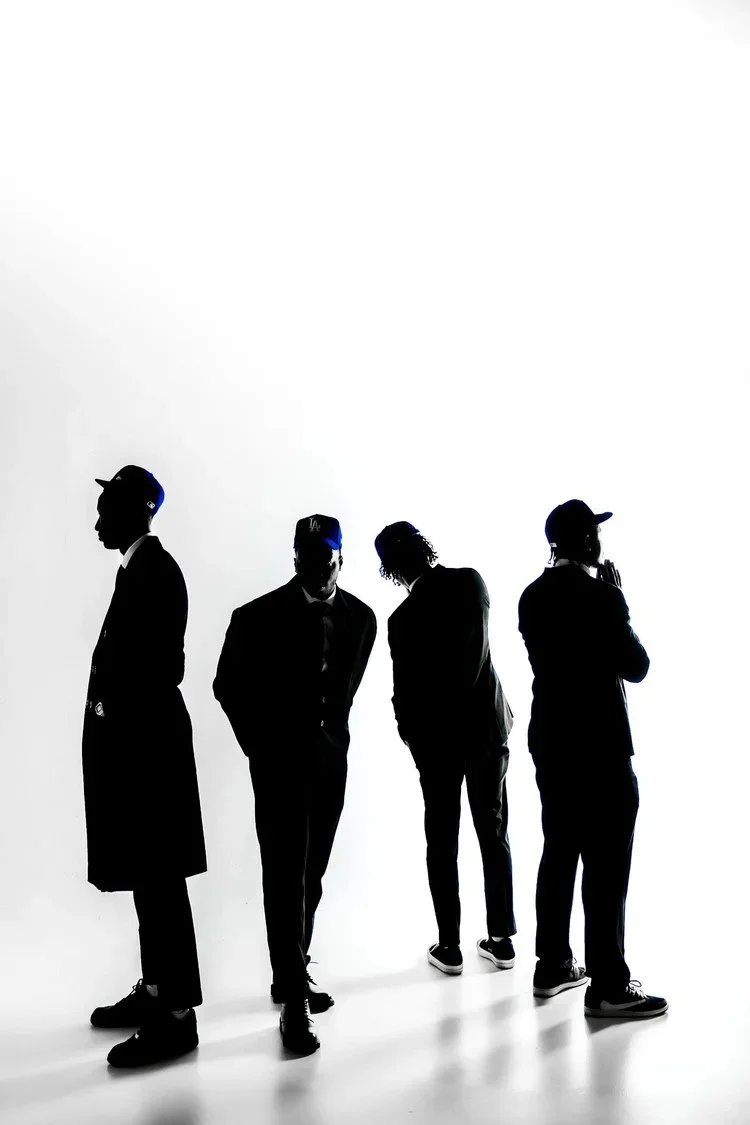 Four silhouettes in suits and caps against a white studio backdrop in Dodger Blue. Photography by Yonathan Mesfun.