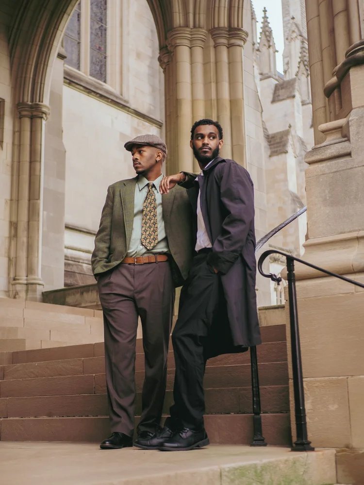 Two models in coats and flat caps stand on church steps in Gentlemen. Photography by Yonathan Mesfun.