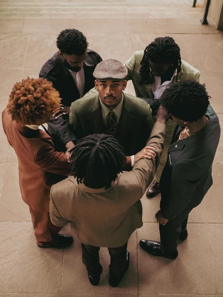 Overhead view of six suited models gathered in a circle in Gentlemen. Photography by Yonathan Mesfun.
