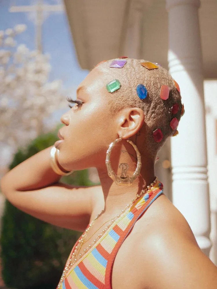 Profile portrait with colorful gems on cropped hair and large hoop earrings in Ghetto Visionary. Photography by Yonathan Mesfun.