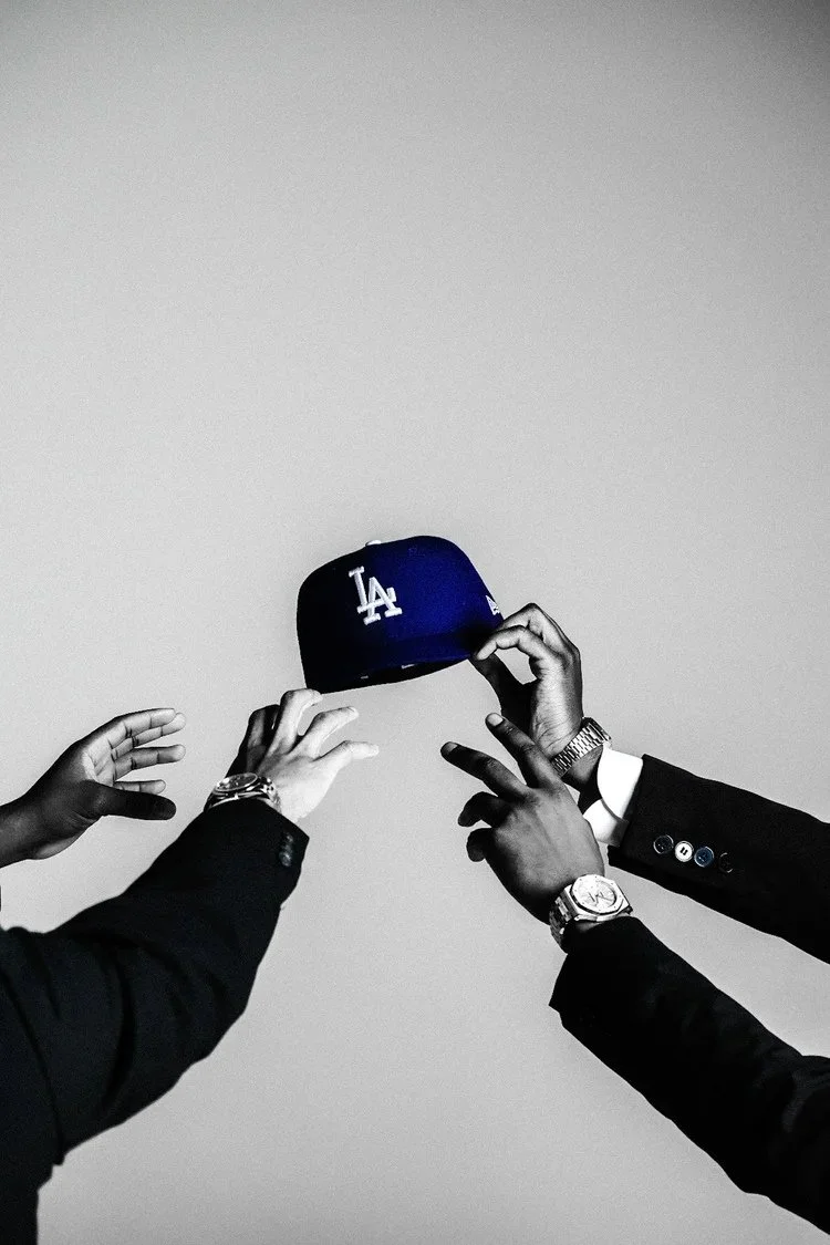 Hands reaching toward a blue LA cap against a monochrome studio background in Dodger Blue. Photography by Yonathan Mesfun.