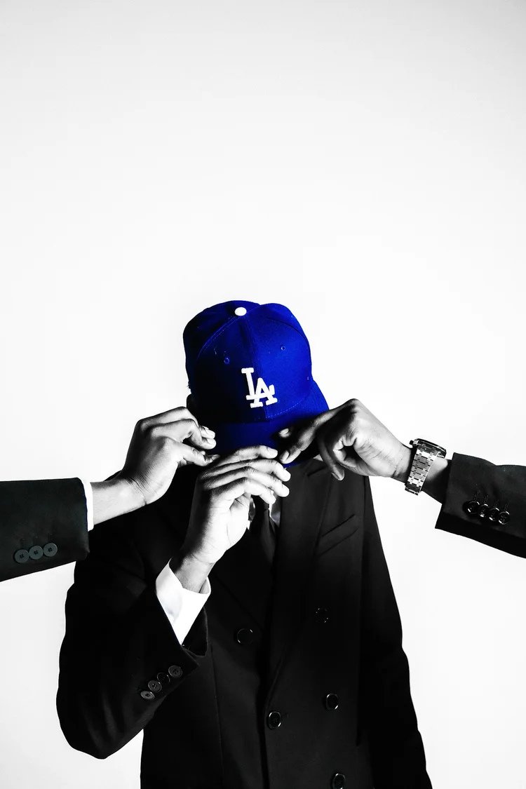 A suited model adjusts a blue LA cap as hands reach into the frame in Dodger Blue. Photography by Yonathan Mesfun.