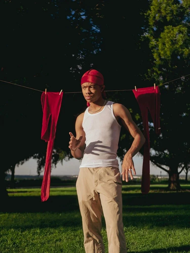 Model in a red durag and white tank top poses beside a clothesline in Durag Drag. Photography by Yonathan Mesfun.