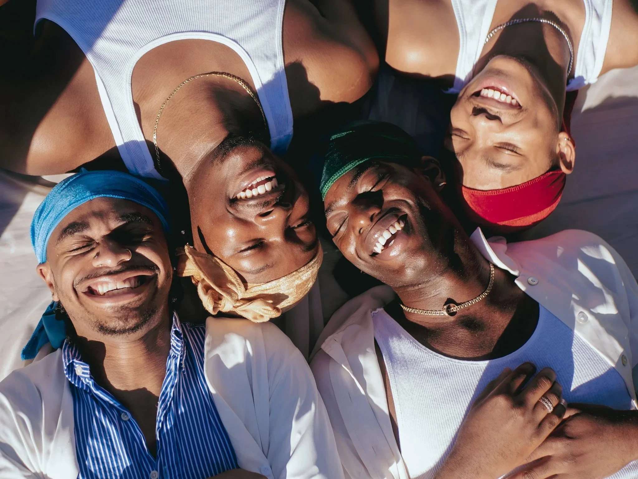 Friends wearing colorful durags smile together in a circular overhead portrait in Durag Drag. Photography by Yonathan Mesfun.