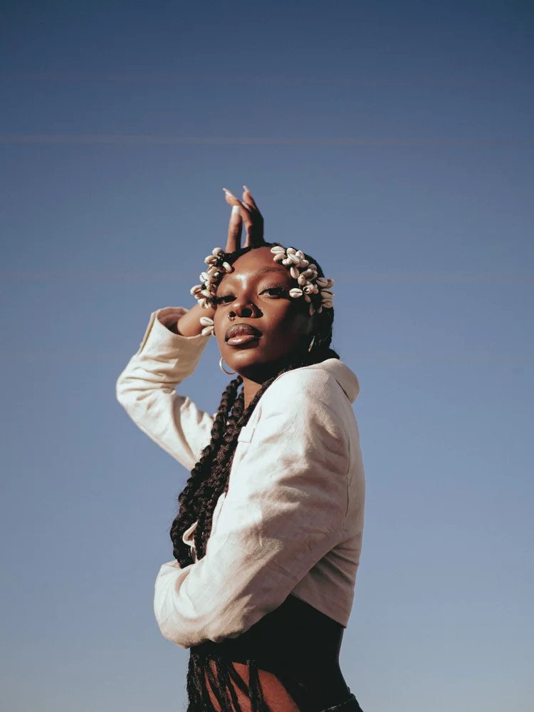 Woman with decorated braids poses beneath a blue sky in Bad Bandits. Photography by Yonathan Mesfun.