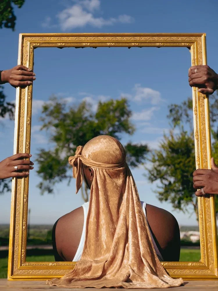 Back view of a gold durag framed by a large gold picture frame outdoors in Durag Drag. Photography by Yonathan Mesfun.