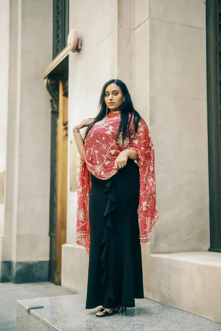 A woman in a black dress and red embroidered shawl poses in a stone doorway in A Collected Culture Pt.2. Photography by Yonathan Mesfun.