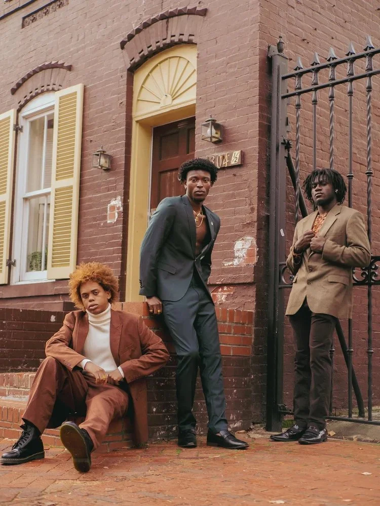 Three models in tailored suits pose beside a brick townhouse in Gentlemen. Photography by Yonathan Mesfun.