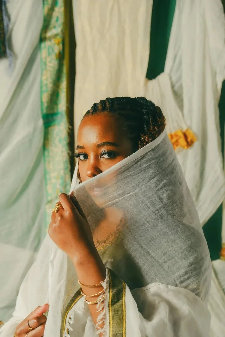 Woman lifts sheer white fabric over the lower half of her face in Netela on Netela. Photography by Yonathan Mesfun.