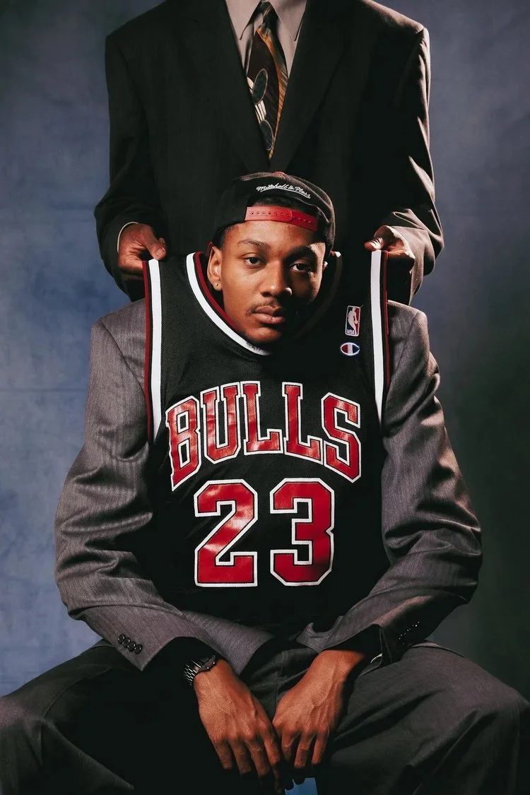 Seated model in a dark suit holds a Bulls number 23 jersey in Draft Day. Photography by Yonathan Mesfun.